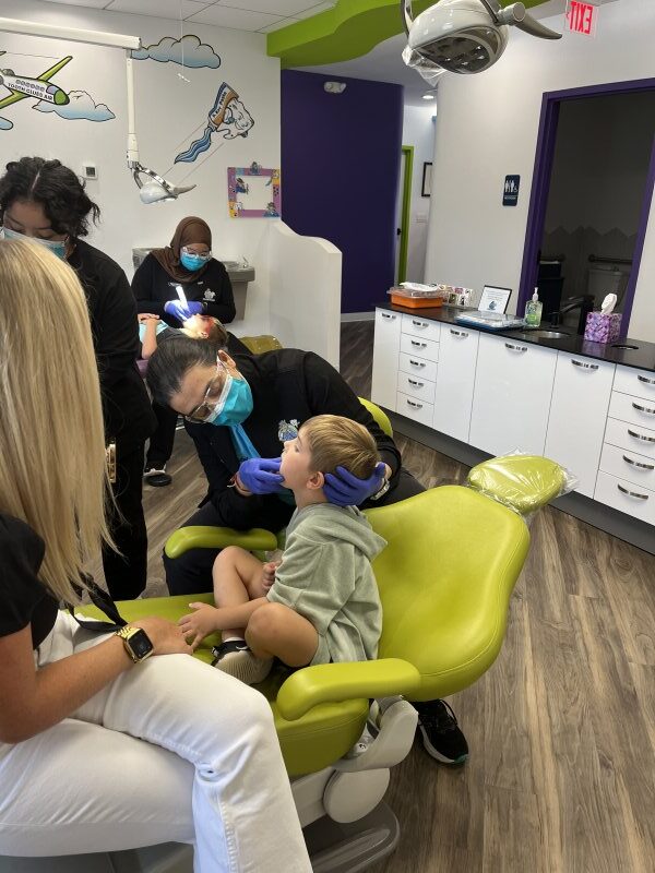 a parent sitting on a treatment chair as Dr. Takiar examines a patient's mouth