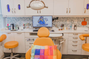 a dental chair with a colorful pillow and a monitor behind it displaying the Tooth Clues logo